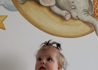 Baby ligt onder muurschildering van olifant en giraffe.